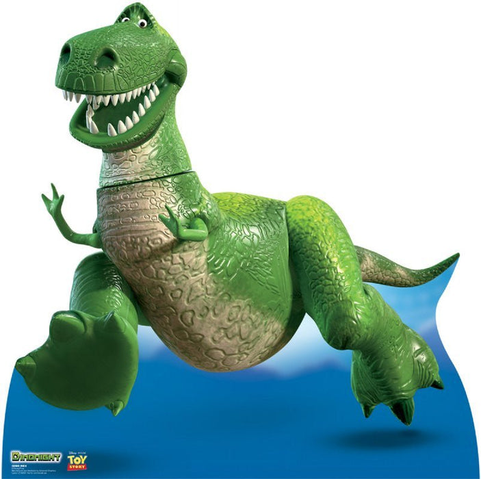 Life-size cardboard cutout of a cheerful green cartoon dinosaur with a big toothy grin and textured scales, mid-run with one foot lifted. The background shows a blue sky with clouds. Logos for 'Disney·Pixar' and 'Toy Story' are displayed in the corner.