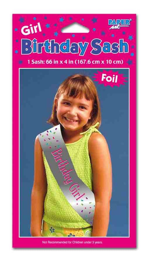 Girl's birthday sash packaging showing a young girl wearing a shiny silver sash with pink text that reads 'Birthday Girl' and colorful confetti graphics. The packaging is bright pink with star decorations and states the sash size as 66 in x 4 in (167.6 cm x 10 cm), labeled as foil and not recommended for children under 3 years.