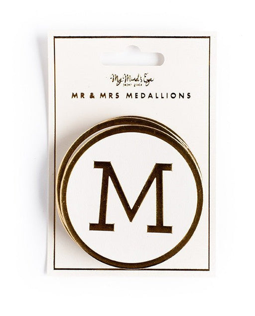 Packaged set of Mr & Mrs medallions by My Mind’s Eye, featuring a circular white medallion with a bold black letter 'M' outlined in gold.