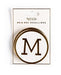 Packaged set of Mr & Mrs medallions by My Mind’s Eye, featuring a circular white medallion with a bold black letter 'M' outlined in gold.