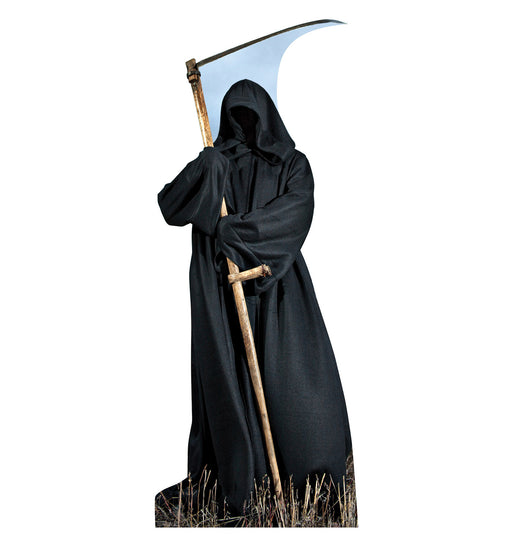 Life-size cardboard cutout of a hooded grim reaper figure dressed in a long black robe, standing in dry grass and holding a large scythe with a curved silver blade