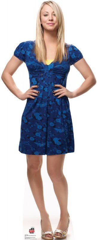 Life-size cardboard cutout of a woman with long blonde hair wearing a blue floral dress and silver peep-toe heels, standing confidently with hands resting on her hips and a slight smile.