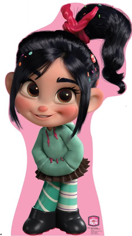 Life-size cardboard cutout of a cheerful animated girl with large brown eyes and black hair tied up in a high ponytail with a red licorice scrunchie. She wears a mint green hoodie, a brown skirt, striped green tights, and black boots. Colorful candy pieces are sprinkled in her hair, and she stands shyly against a pink background.
