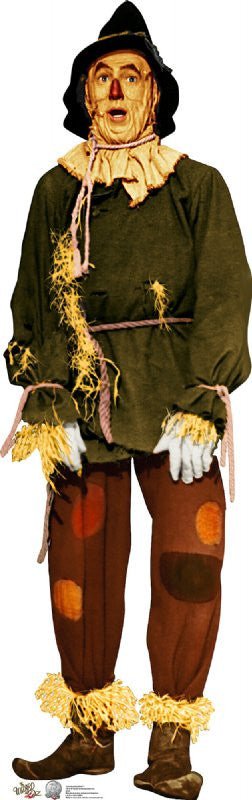 Scarecrow character dressed in a forest green tunic with a beige rope belt, brown pants featuring orange, rust, and tan patches, and straw protruding from his sleeves, collar, and pant cuffs. He wears a black floppy hat, pale blue gloves, and brown shoes, completing his rustic and whimsical appearance.
