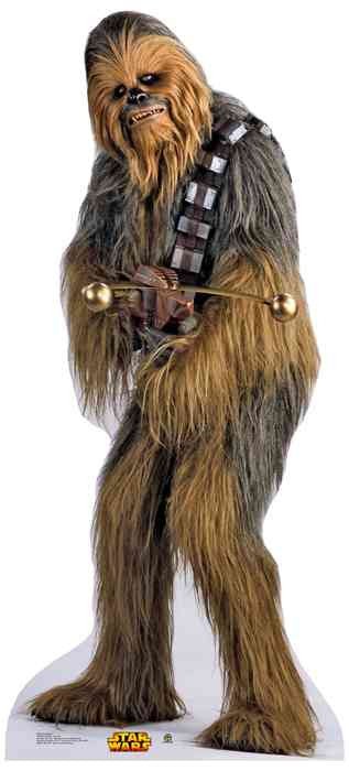 Life-size cardboard cutout of Chewbacca from Star Wars, covered in long shaggy fur that blends shades of dark brown, gray, and golden tan. He wears a bandolier with metallic squares and is holding his signature bowcaster weapon. The cutout stands on a white base featuring the yellow and red Star Wars logo.