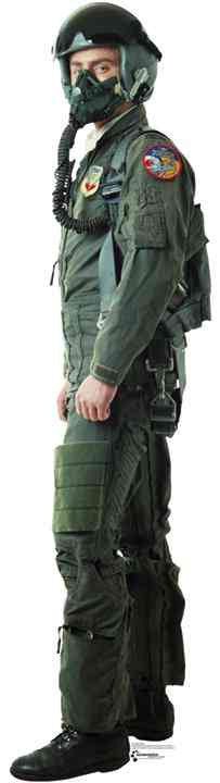 Cut-out of a fighter pilot in full green flight suit with helmet, oxygen mask, and tactical gear, standing in a side-facing pose. Patches and insignia are visible on the arms and chest, and the pilot is wearing black boots.