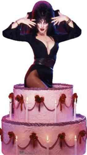 Cut-out of Elvira, Mistress of the Dark, dramatically posing with hands raised near her face while emerging from a large, pink tiered cake decorated with red bows, draped icing, and lit white candles. She is dressed in her signature black, form-fitting gown with a high slit and plunging neckline.