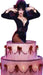 Cut-out of Elvira, Mistress of the Dark, dramatically posing with hands raised near her face while emerging from a large, pink tiered cake decorated with red bows, draped icing, and lit white candles. She is dressed in her signature black, form-fitting gown with a high slit and plunging neckline.