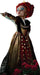 A woman with bright red hair styled high, wearing a gold, black, and red gown with heart patterns and dramatic blue eyeshadow, pointing with an outstretched arm.