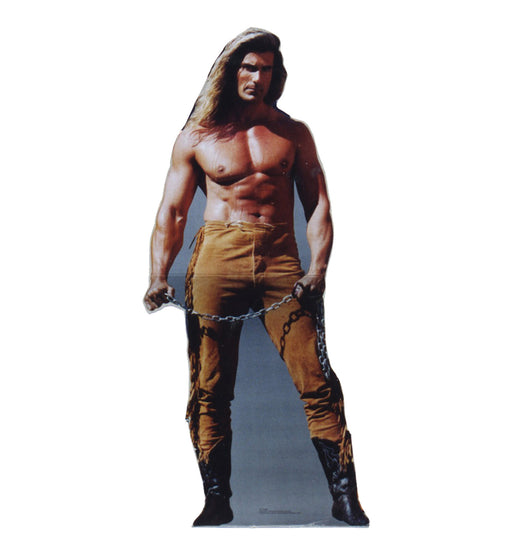 A life-size cutout of a muscular shirtless man with long brown hair, wearing tan pants with fringe, black boots, and holding a chain in both hands.