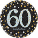 Black round plate with a large light blue glittery number '60' in the center, surrounded by gold, silver, and white confetti dots, with the words 'happy birthday' in lowercase script below the number.