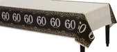 Rectangular table covered with a white tablecloth featuring a black border patterned with the number '60' in white and scattered gold and silver dots, celebrating a 60th birthday