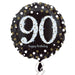 Round black foil balloon with large silver glitter-effect number '90' in the center, surrounded by gold and silver confetti dots, and the words 'happy birthday' in small white script below.