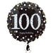 Round black foil balloon with large silver glitter-effect number '100' in the center, surrounded by gold and silver confetti dots, and the words 'happy birthday' in small white script below.
