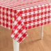 Rectangular table cover with a red and white gingham pattern, featuring alternating squares decorated with small white or red floral motifs, draped over a wooden table.
