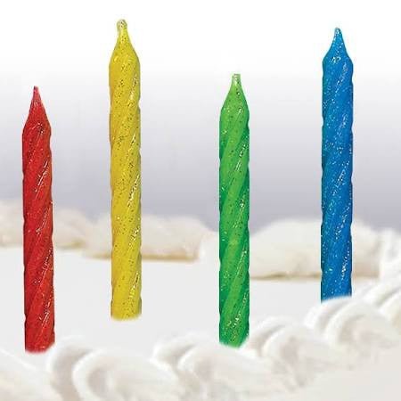 Four spiral birthday candles in red, yellow, green, and blue, standing upright on a white frosted cake.