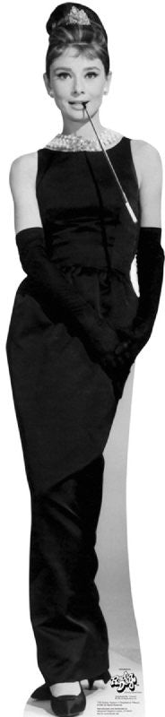 Life-size cardboard cutout in black and white of a glamorous woman in a classic black evening gown with a pearl necklace, long black gloves, and a tiara, holding a cigarette holder elegantly between her lips.
