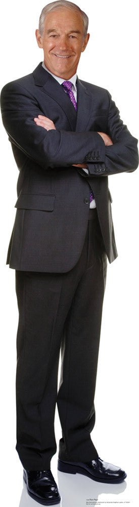 Life-size cardboard cutout of an older man with short gray hair, wearing a dark charcoal suit, white dress shirt, and purple patterned tie, standing confidently with arms crossed and a friendly smile.