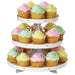 Three-tier white cardboard cupcake stand holding yellow cupcakes with pastel frosting in pink, green, and yellow, arranged in a circular display.
