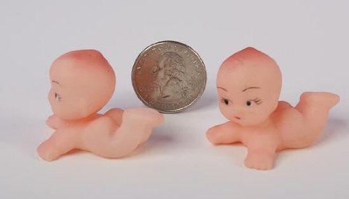 Two small, peach-colored crawling baby figurines with painted facial features, shown beside a quarter for size comparison.
