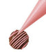 Pink icing being piped in fine lines over a round chocolate truffle using a piping bag.