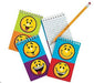 A set of mini spiral notepads with bold, two-tone covers in orange, green, blue, red, and purple. Each pad features two large yellow smiley faces with playful expressions—grinning, winking, or tongue out. Includes lined pages and a sharpened yellow pencil with red eraser.