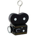Movie camera-themed balloon or card holder designed to resemble a vintage black film camera with white and silver lens details and yellow accent lines. A metal wire extends upward from the top, ending in a circular clip for holding balloons, photos, or cards.
