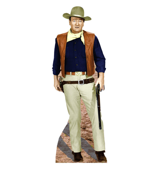 Life-size cutout of a classic cowboy figure dressed in a tan wide-brimmed hat, navy blue shirt, tan pants, and brown leather vest. He wears a light yellow neckerchief and brown boots, with a gun holstered at his waist and a lever-action rifle held in his right hand. The base shows a dusty western terrain.