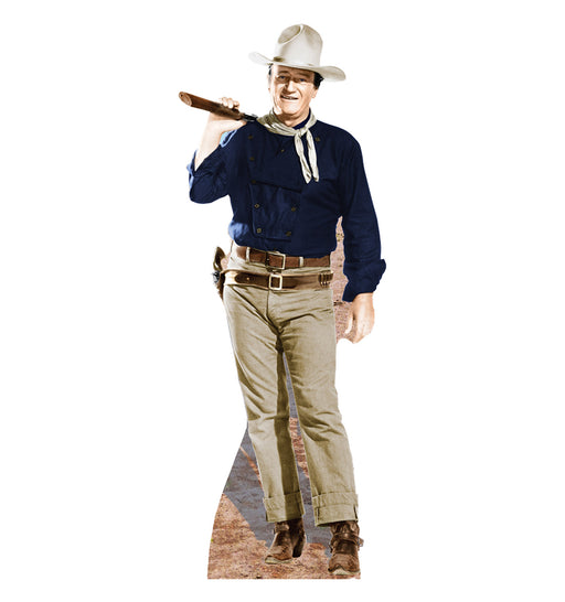 Life-size cutout of a cowboy wearing a white hat, dark blue shirt, light tan pants, brown belt with a holster, and brown boots. He has a light-colored scarf tied around his neck and is smiling while resting a rifle over his right shoulder. The base features a dusty western ground.