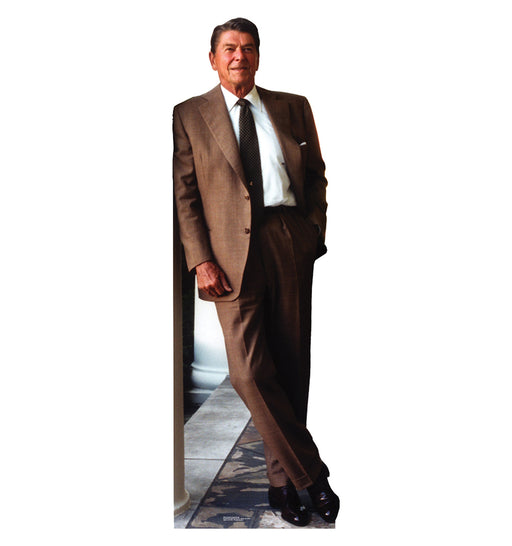 Cardboard cutout of Ronald Reagan in a relaxed pose, leaning casually against a white column. He is dressed in a brown suit with a white dress shirt and dark patterned tie, with his legs crossed and one hand in his pocket. The floor beneath him is tiled and partly carpeted.