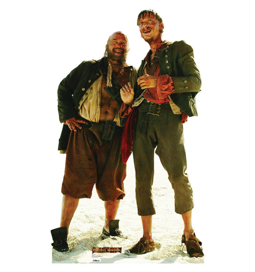 Cardboard cutout of two scruffy pirates from Pirates of the Caribbean, standing barefoot on a sandy beach. The pirate on the left is bald with a thick beard, wearing a black open jacket and brown shorts with a wide belt. The pirate on the right is thinner, with messy hair, a greenish jacket, and tattered brown pants, holding a bottle and grinning. Both appear dirty and disheveled, with sunburned faces and carefree expressions.