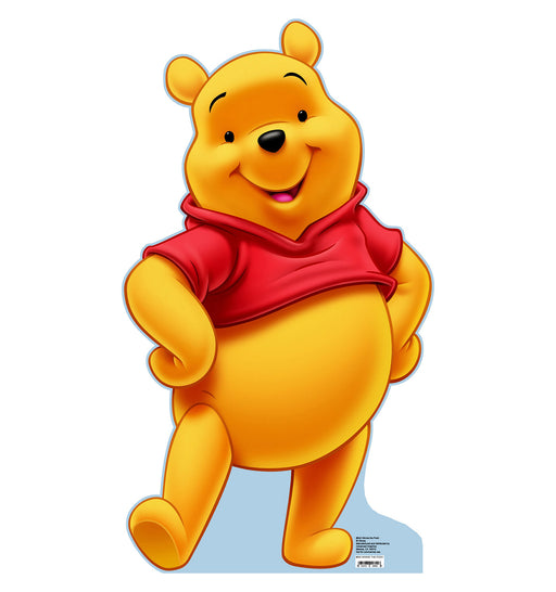 Cardboard cutout of Winnie the Pooh standing in a cheerful pose. Pooh is a plump, golden-yellow bear with rounded ears and black eyes. He is wearing his signature short red shirt, which leaves his belly exposed. One arm is resting on his hip while the other swings outward, and his mouth is open in a friendly smile. The background is white with a blue shadow beneath his feet.
