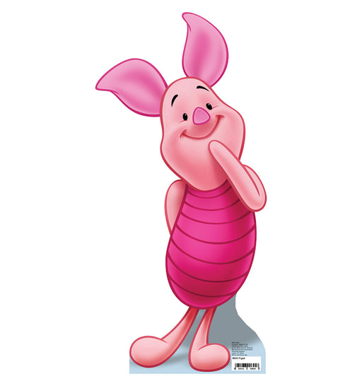 Cardboard cutout of Piglet from Winnie the Pooh, shown standing with one hand shyly placed on his cheek and a sweet smile. His body is light pink, and he wears a darker pink striped outfit. His large ears curve gently with bright pink inner coloring. He stands with one leg crossed over the other, casting a soft shadow onto the light blue base beneath him against a white background.