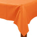 Orange rectangular plastic table cover draped over the corner of a wooden table, with visible folds and a glossy finish.