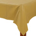 Rectangular gold plastic table cover draped over a wooden table corner, featuring subtle folds and a soft sheen finish.