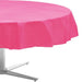 Round table covered with a bright pink plastic tablecloth, hanging evenly over the edges, with part of a metal table base visible underneath.