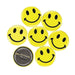Seven round yellow buttons with black smiley face designs arranged on a white background. One button is flipped to show the silver metal pin backing with a safety clasp.