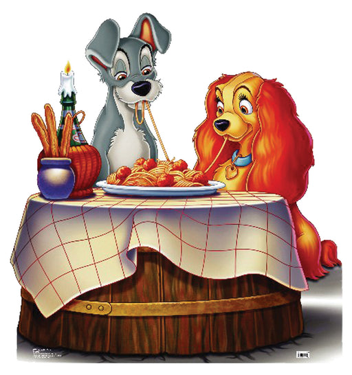 Cut-out of Lady and the Tramp, the animated dogs, sharing a romantic spaghetti dinner at a round wooden table covered with a white tablecloth featuring red grid lines. Tramp, a gray dog with floppy ears, and Lady, a brown and tan cocker spaniel with long ears, are slurping the same strand of spaghetti. A candle in a wine bottle and a breadstick basket sit on the table, creating a cozy, charming atmosphere.