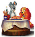 Cut-out of Lady and the Tramp, the animated dogs, sharing a romantic spaghetti dinner at a round wooden table covered with a white tablecloth featuring red grid lines. Tramp, a gray dog with floppy ears, and Lady, a brown and tan cocker spaniel with long ears, are slurping the same strand of spaghetti. A candle in a wine bottle and a breadstick basket sit on the table, creating a cozy, charming atmosphere.