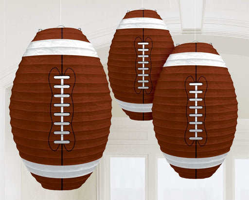 Three hanging paper lanterns shaped like American footballs, featuring a brown textured design with white laces and white stripes on each end, suspended from the ceiling in a bright room.