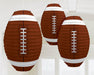 Three hanging paper lanterns shaped like American footballs, featuring a brown textured design with white laces and white stripes on each end, suspended from the ceiling in a bright room.
