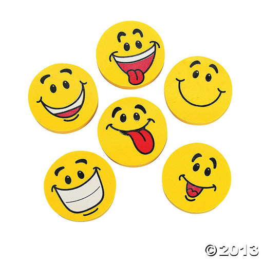 A set of six round, yellow smiley face erasers, each with a playful expression. One shows a big open smile with a tongue out, another has a simple closed-mouth smile. One features a wide toothy grin, while another sticks its tongue out to the side with a cheeky smile. One has a tilted smirk with a raised eyebrow, and another shows a happy open-mouth grin with a tongue showing.