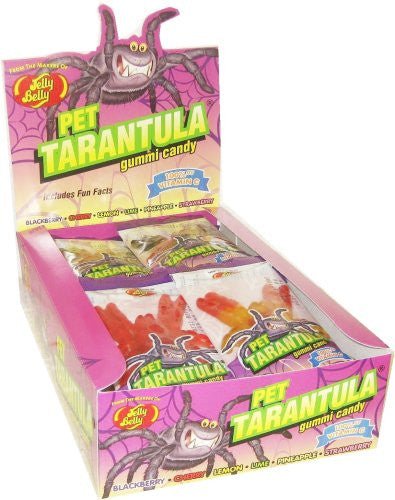 Box display of Jelly Belly Pet Tarantula gummy candy. The packaging is bright pink and purple with a cartoon tarantula illustration. The front shows individual gummy packs in assorted colors and flavors such as blackberry, cherry, lemon, lime, pineapple, and strawberry.