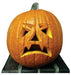 A carved orange pumpkin with an angry expression, featuring slanted triangle eyes, a jagged nose, and a frowning mouth with sharp teeth, sitting on a striped platform.