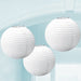 Three round white paper lanterns with ribbed texture, hanging from thin strings against a light blue background.
