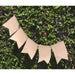 String of five natural burlap pennant flags with a swallowtail cut, hanging on a twine rope against a leafy green background.