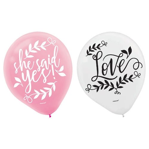 One pink balloon with the words ‘she said yes!’ in white script surrounded by leafy accents, next to a white balloon with the word ‘Love’ in black script with leafy decorations.