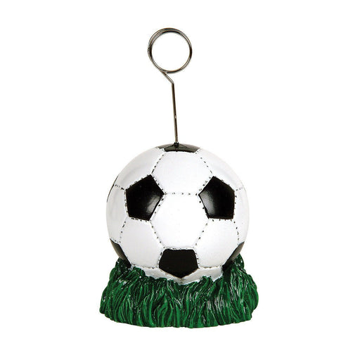 Soccer-themed card or balloon holder featuring a black and white soccer ball resting on a green grass-like base, with a metal wire holder extending upward and ending in a circular clip.