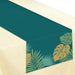 Dark teal table runner with tropical leaf designs in green and gold at the ends, displayed on a cream-colored tablecloth.