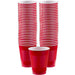 A set of red plastic party cups stacked in three tall columns, with approximately 50 cups in total. The cups are standard size, with a white interior and ridged exterior for grip. Two shorter stacks appear in the front, emphasizing the volume and design of the cups. The image showcases the product in bulk, ideal for large gatherings or events, and conveys durability and uniformity through consistent stacking.